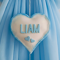 Dettaglio del nome Liam in stampatello azzurro su pendente a forma di cuore del fiocco nascita categoria DOLCEZZA.